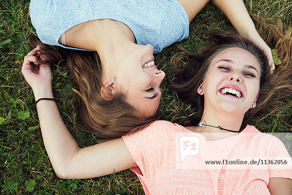 Portrait von zwei jungen Frauen  die im Gras liegen und lachen
