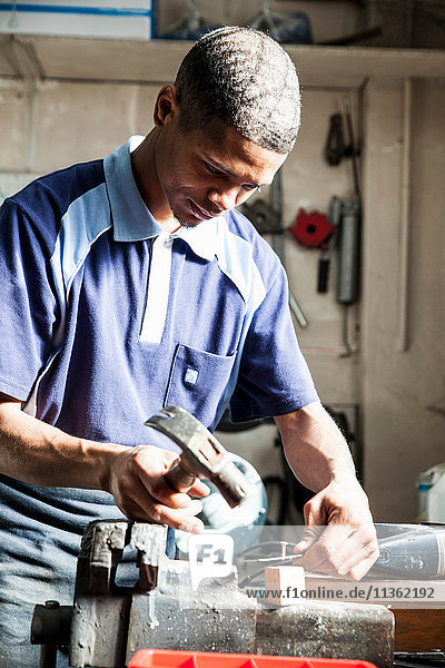 Young man hammering nail in repair workshop