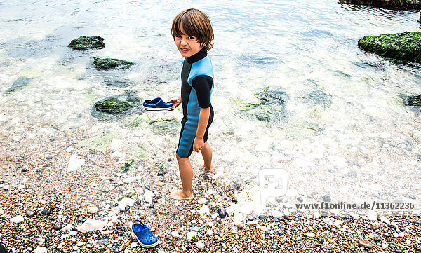 Boy ankle deep in water holding shoe