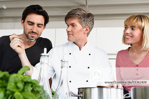 Chef and couple in kitchen tasting food