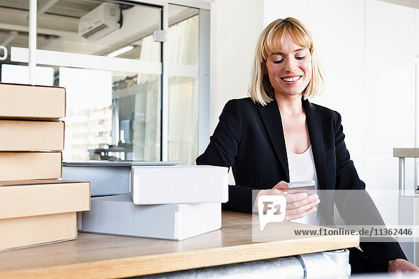 Geschäftsfrau im Büro schaut lächelnd auf Smartphone