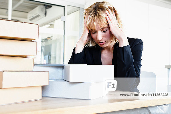 Geschäftsfrau mit einem Stapel Bücher  Kopf in Händen  die gestresst aussehen
