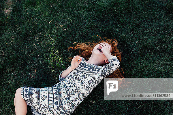 High angle view of girl lying on grass covering face laughing
