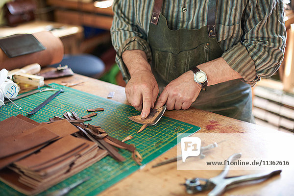 Männlicher Arbeiter in Lederwerkstatt  Überprüfung der Schärfe des Messers auf Leder  Mittelteil