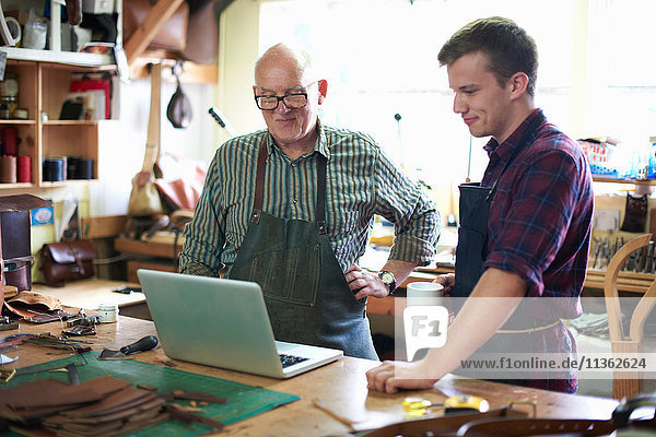 Zwei männliche Arbeiter in der Lederwerkstatt  Blick auf Laptop