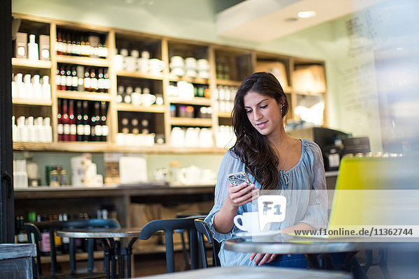 Junge Frau liest Smartphone-Texte im Cafe