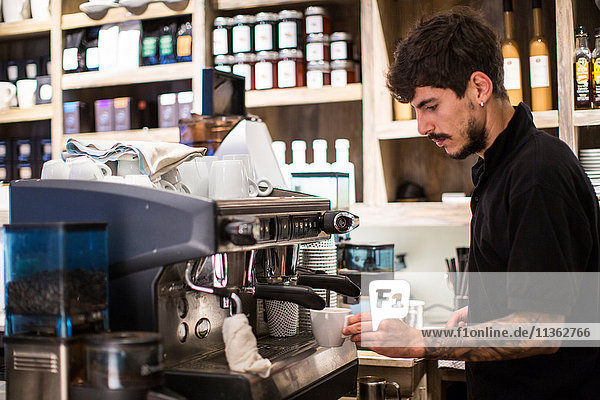 Junger männlicher Barista benutzt Kaffeemaschine im Café
