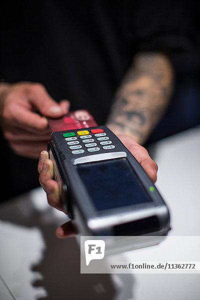 Nahaufnahme der Hände eines jungen Mannes am Kreditkartenautomaten