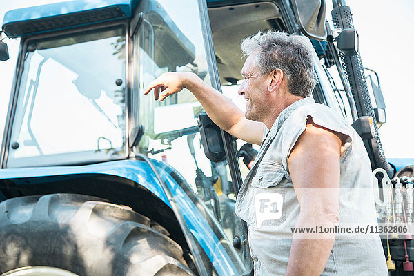 Älterer männlicher Landwirt lehnt an Traktor