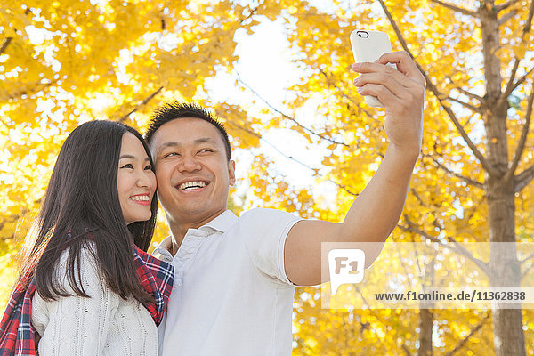 Junges Paar beim Smartphone-Selfie im Herbstpark Peking China