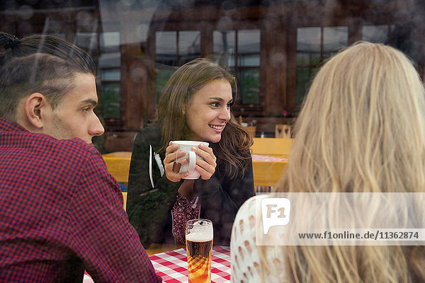 Drei junge erwachsene Freunde mit Kräutertee und Bier im Cafe