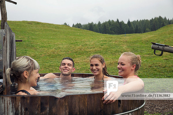 Vier erwachsene Freunde lachen beim Entspannen im ländlichen Whirlpool  Sattelbergalm  Tirol  Österreich