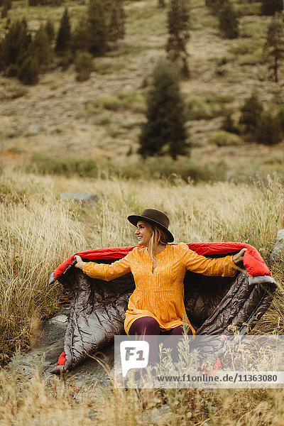 Frau sitzt in ländlicher Umgebung  in einen Schlafsack gehüllt  Mineral King  Sequoia National Park  Kalifornien  USA