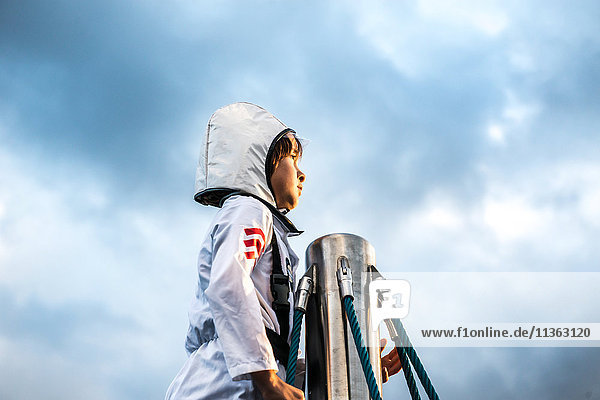 Porträt eines Jungen im Astronautenkostüm  der von der Spitze des Klettergerüstes gegen den dramatischen Himmel blickt
