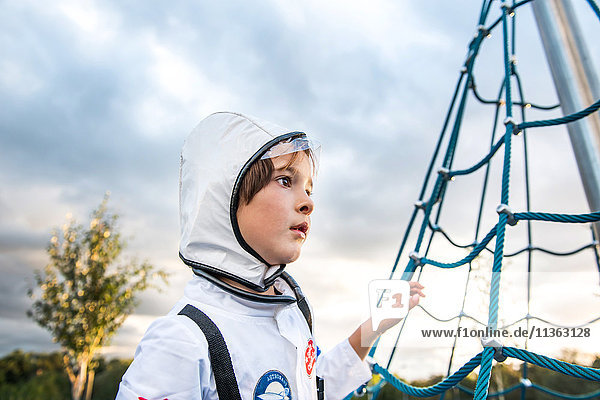 Porträt eines Jungen in Astronautenkostüm  der am Klettergerüst des Spielplatzes vorbeischaut