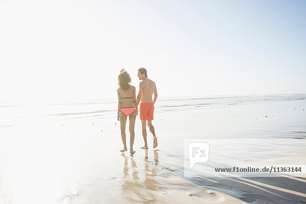 Rear view of young couple in swimwear strolling on sunlit beach  Cape Town  Western Cape  South Africa