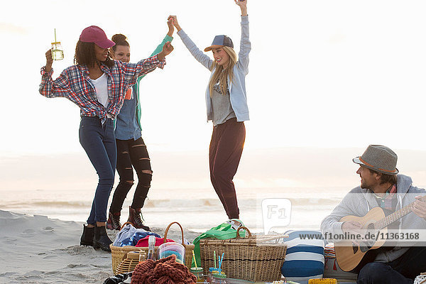 Young man playing guitar and female friends dancing at beach  Cape Town  Western Cape  South Africa