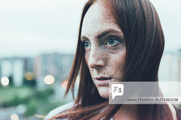 Nahaufnahme Porträt einer jungen sommersprossigen Frau mit langen roten Haaren und Nasenpiercing