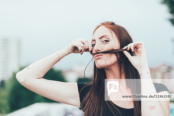 Porträt einer jungen Frau mit Sommersprossen  die einen Schnurrbart mit langen roten Haaren macht.