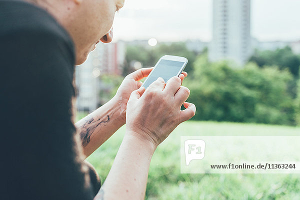 Abgeschnittene Aufnahme einer Frau auf Rasen mit Smartphone-Touchscreen