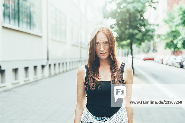 Porträt einer sommersprossigen jungen Frau mit langen roten Haaren auf der Stadtstraße stehend
