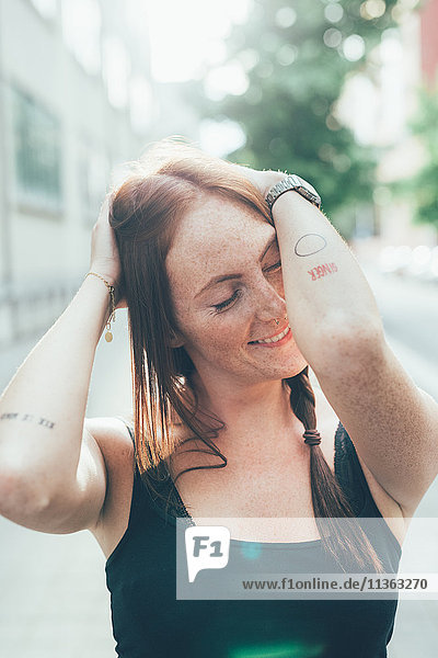 Young woman with long red hair and freckles with eyes closed on city street