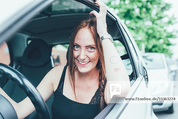 Porträt einer jungen Frau mit langen roten Haaren und Sommersprossen am Autofenster