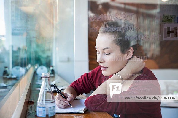 Junge Frau sitzt im Café und schreibt auf einem Notizblock