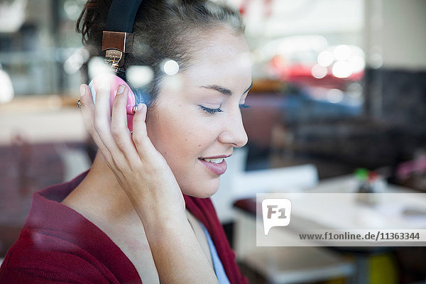 Young woman sitting in cafe  wearing headphones  smiling