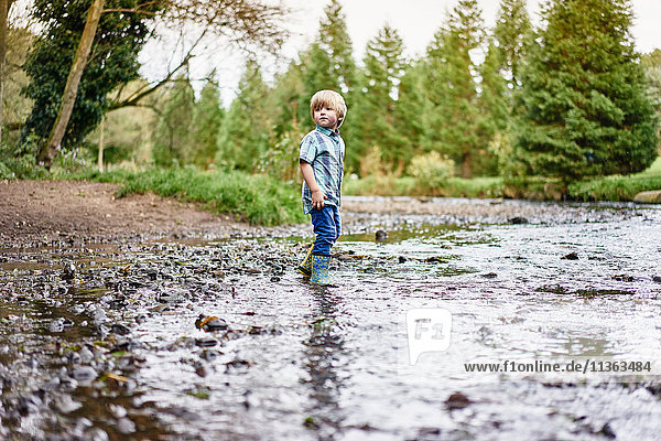 Junge mit Gummistiefeln im seichten Fluss