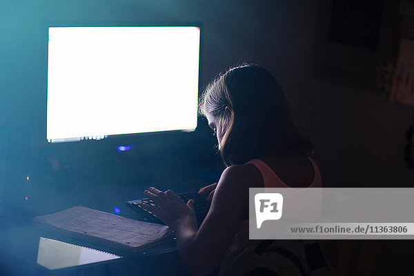 Mädchen benutzt Computer in schwach beleuchtetem Raum