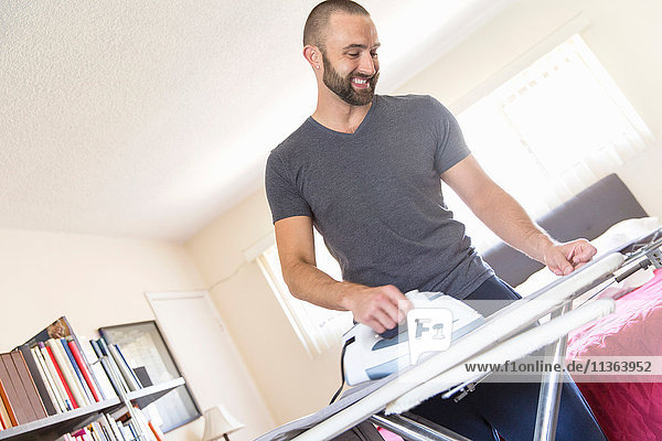 Mittelgroßer erwachsener Mann bügelt Hemd im Wohnzimmer