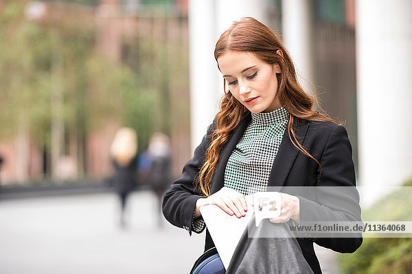 Geschäftsfrau in der Stadt platziert digitales Tablett in der Handtasche