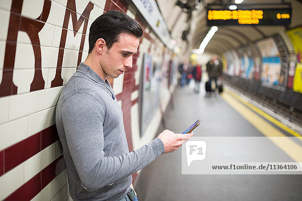 Side view of man on railway platform looking at smartphone