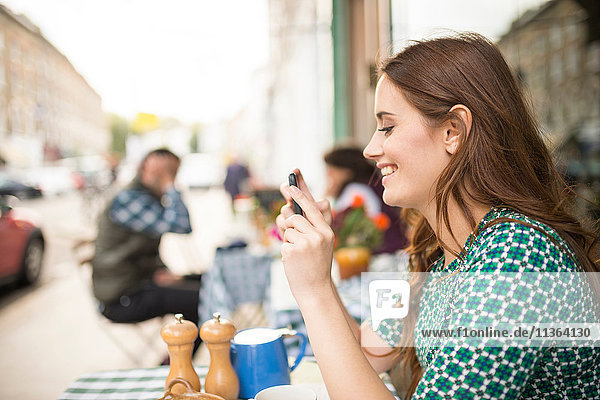 Side view of woman at pavement cafe looking at smartphone smiling
