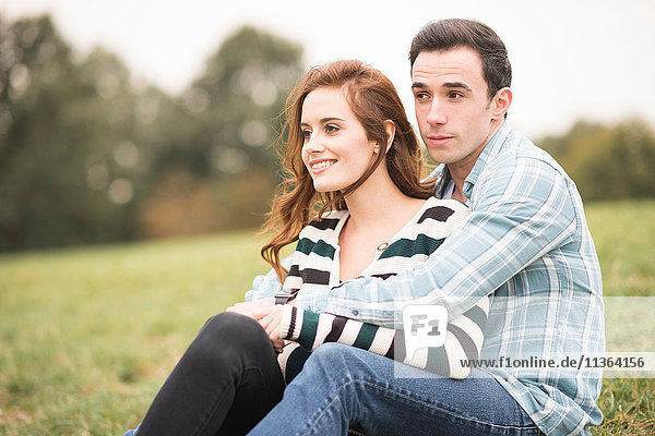Couple sitting in field hugging looking away