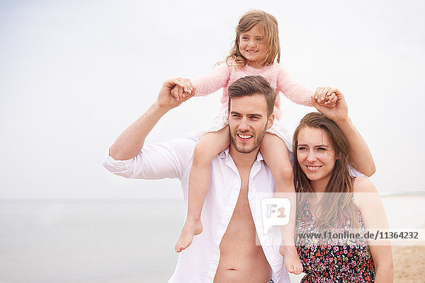 Familie geht am Strand spazieren  Tochter sitzt auf den Schultern des Vaters