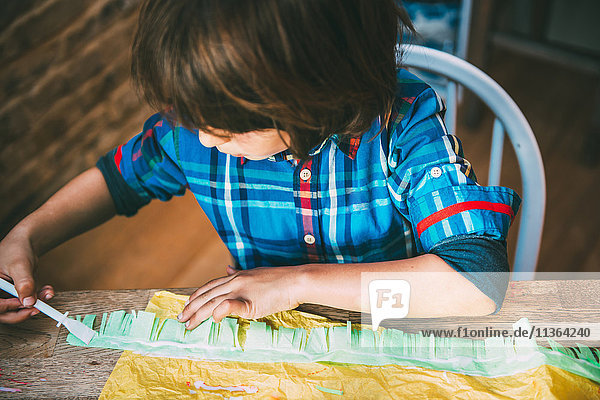 Junge  der Kleber auf Krepppapier aufträgt  um Pinata herzustellen.