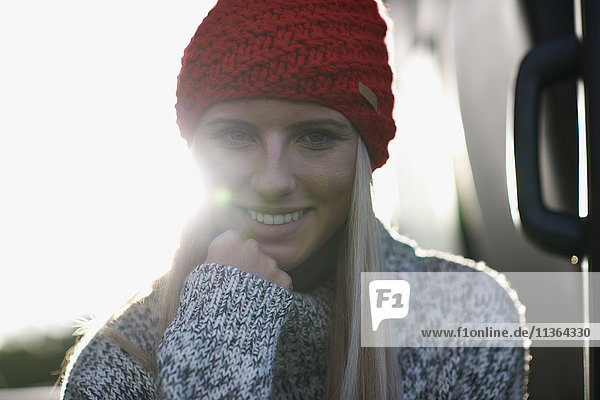 Sunlit portrait of young woman in red knit hat