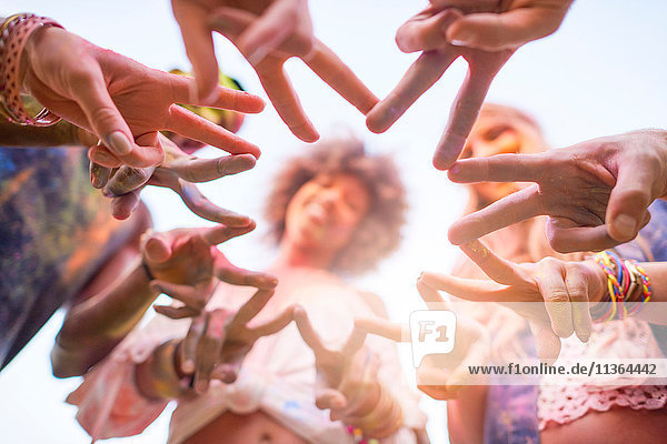 Gruppe von Freunden beim Festival  mit farbenfroher Pulverfarbe bedeckt  Finger mit Friedenszeichen verbinden  Blick aus niedrigem Winkel