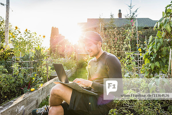 Man typing on laptop in sunlit community garden Vancouver Canada