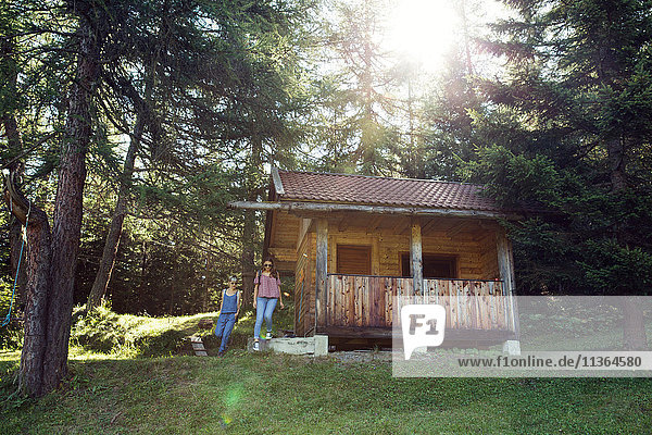 Two female friends leaving log cabin in forest  Sattelbergalm  Tyrol  Austria