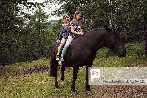 Mädchen und Frau sitzen ohne Sattel auf einem Pferd auf einer Waldlichtung  Sattelbergalm  Tirol  Österreich