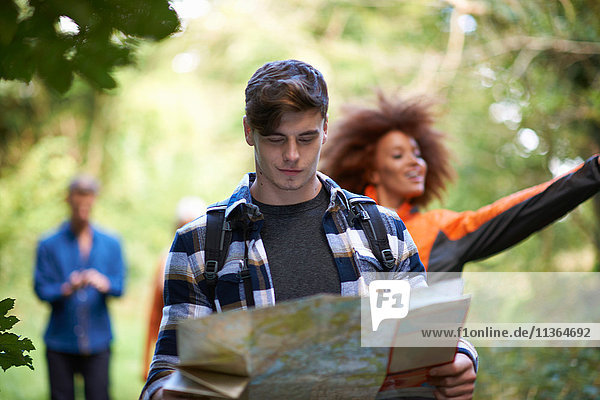 Mann wandert mit Freunden im Wald und schaut auf Karte
