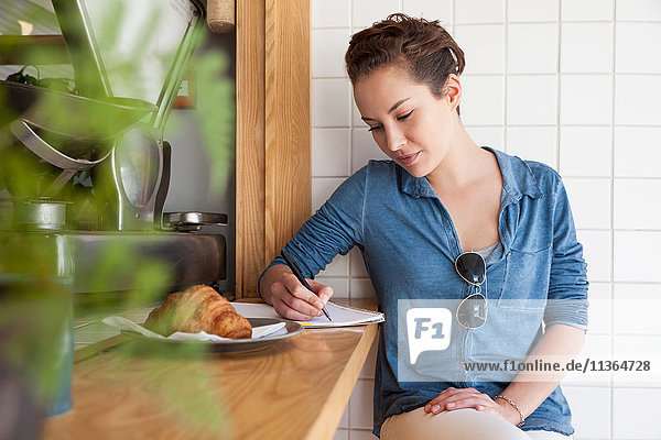 Young woman sitting at bar in cafe  writing notes in notepad