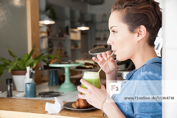 Young woman sitting at bar in cafe  drinking drink through straw