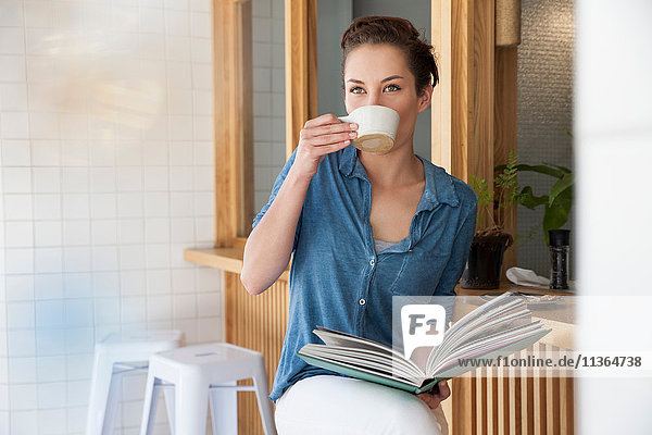 Junge Frau sitzt an der Bar im Café  trinkt Kaffee  hält ein Buch