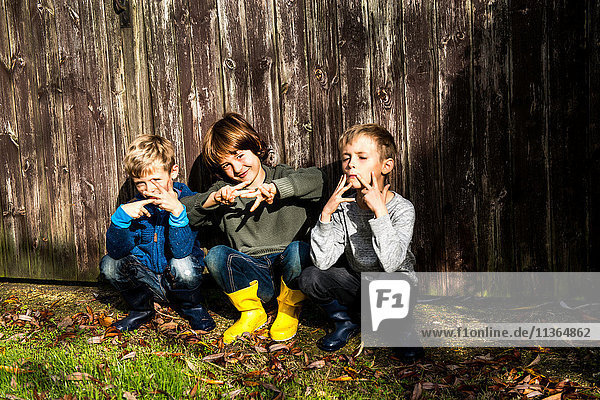 Three boys  outdoors  crouching beside fence  making hand gestures