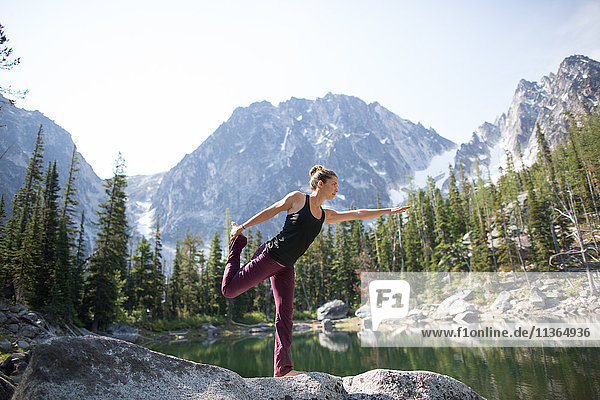 Junge Frau steht auf einem Felsen am See  in Yoga-Pose  Die Verzauberungen  Alpine Lakes Wilderness  Washington  USA