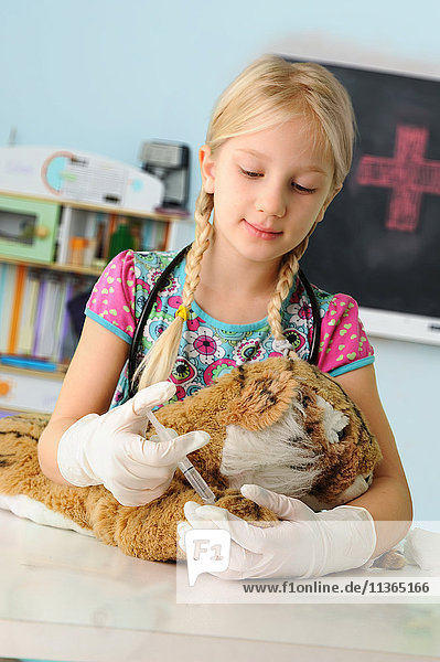 Mädchen  das sich als Tierarzt ausgibt und Spielzeug-Tiger-Spritze injiziert